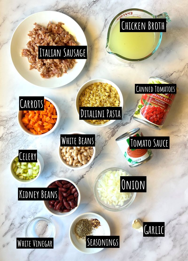 Ingredients displayed for Easy pasta fagioli. Italian sausage, chicken broth, carrots, ditalini pasta, canned tomatoes, white beans, kidney beans, tomato sauce, celery, onion, garlic, seasonings, brown sugar, and white vinegar.
