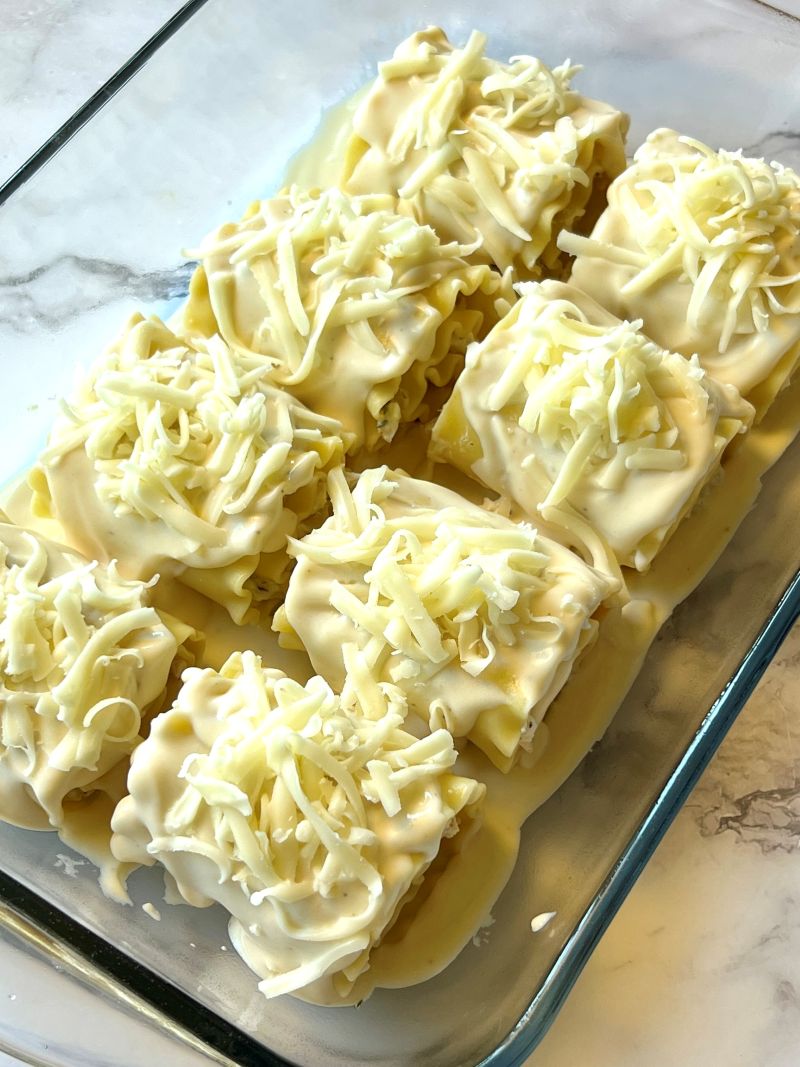 Lasagna rolls placed in the baking dish and topped with alfredo sauce and mozzarella cheese.