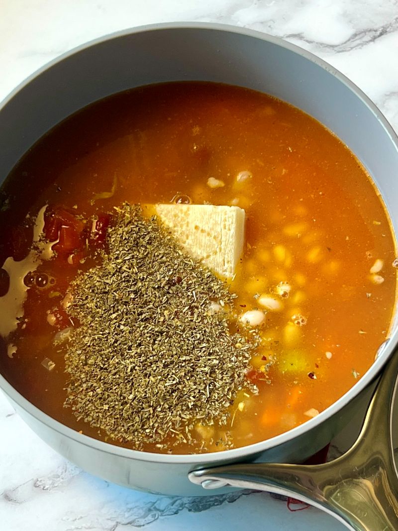 Broth, seasonings, tomato sauce, canned tomatoes, beans, and parmesan cheese rind added to the meat and veggies. 