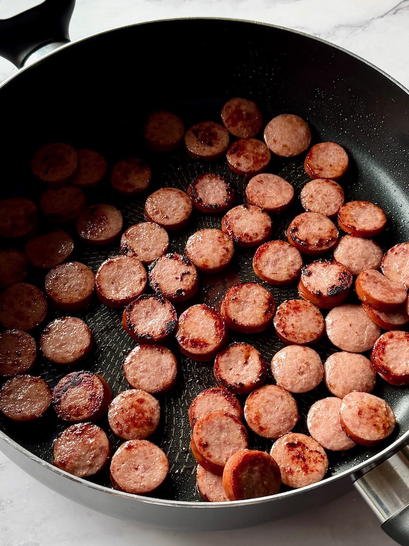 Smoked sausage slices browned in a large skillet.