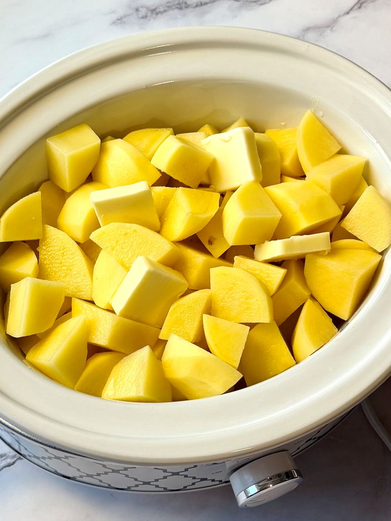 Peeled and cubed potatoes in the slow cooker with butter and chicken broth. 