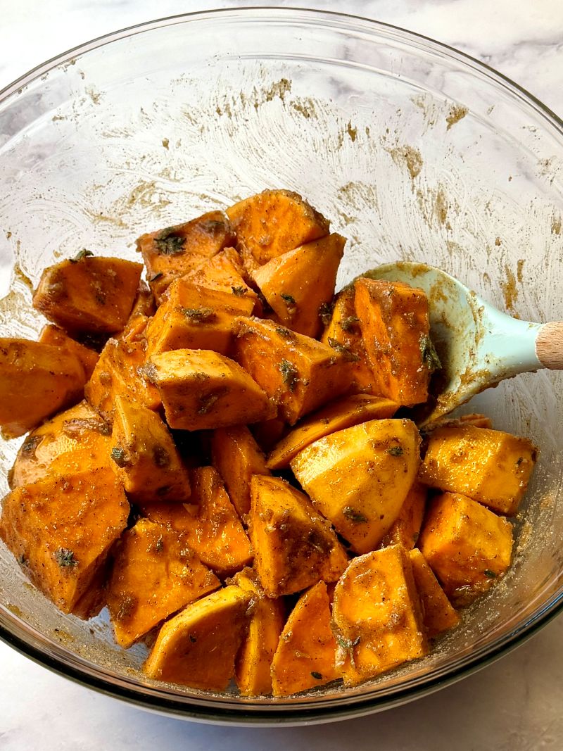 Sweet potatoes chunks combined with butter, brown sugar, fresh thyme, all-spice, salt and pepper in a bowl.