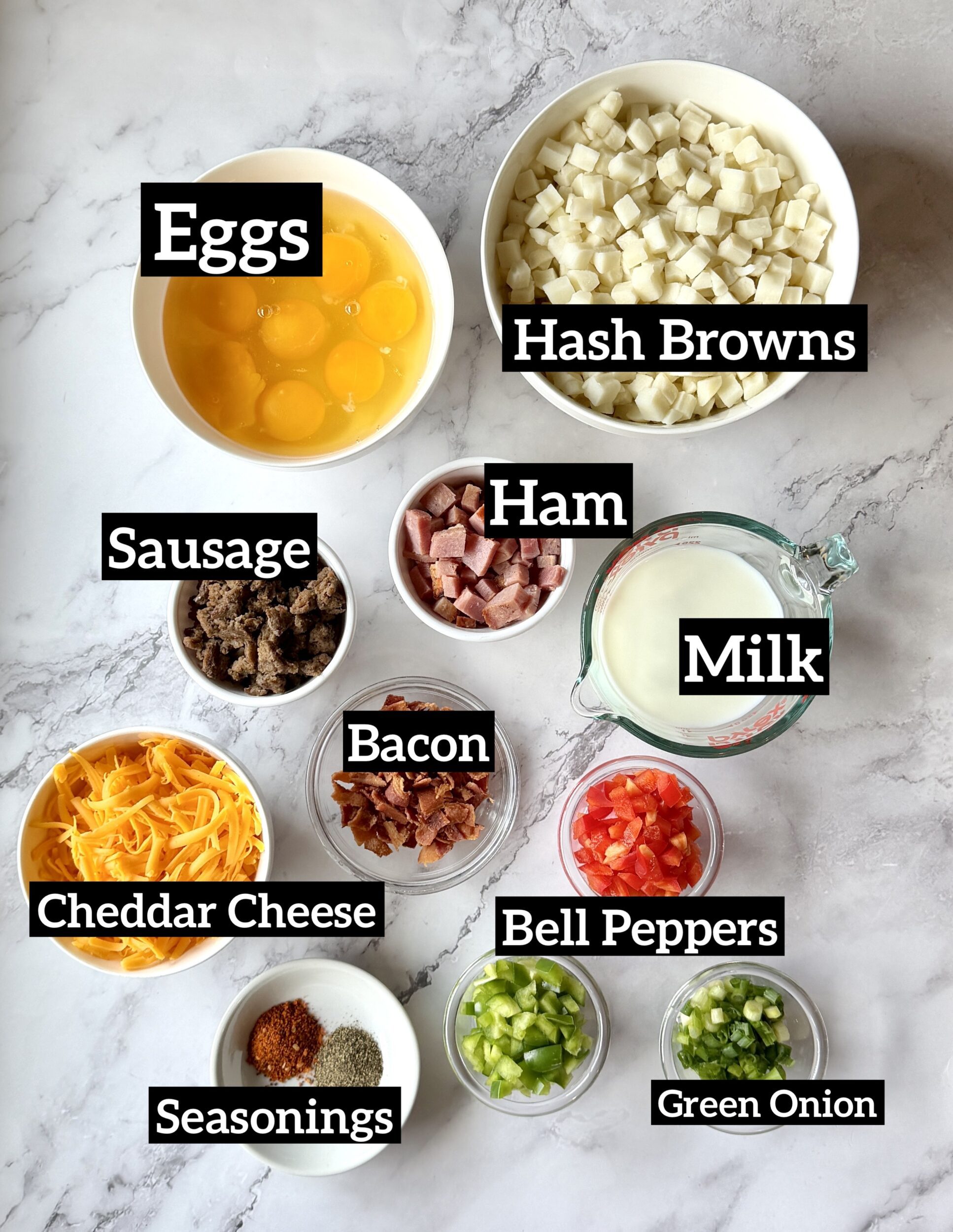 ingredients displayed for farmer's breakfast casserole. Eggs, frozen hash browns, cooked sausage, ham, cooked bacon, bell peppers, green onion, cheddar cheese, milk, seasonings. 