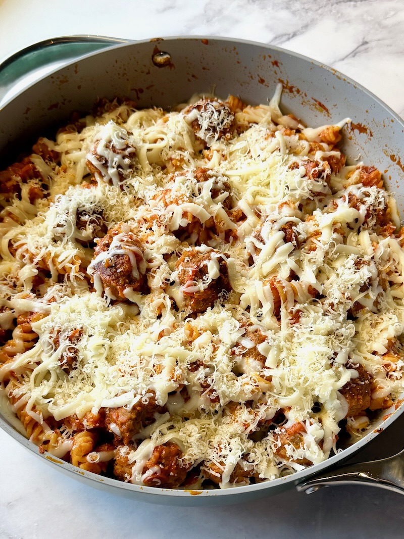 Baked pasta and meatballs, topped with cheese in a skillet. 