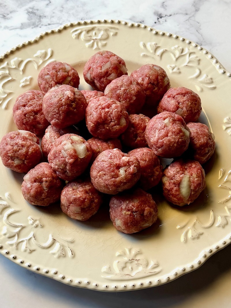 Meatballs formed and resting on a plate. 