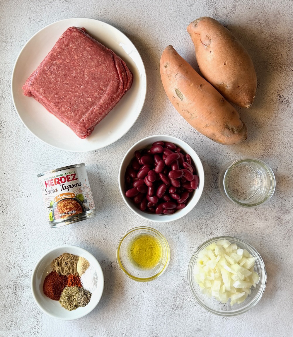 Ingredients displayed for baked sweet potatoes stuffed with taco meat. Ground beef, sweet potatoes, kidney beans, water, salsa, oil, onions, taco seasonings. 