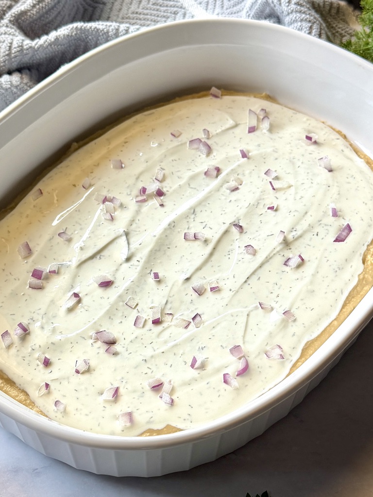 Medium shallow dish with a layer of hummus, tzatziki, and red onion.