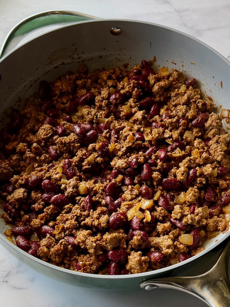 Ground beef mixture cooked in a skillet with onions, beans, spices, and salsa.