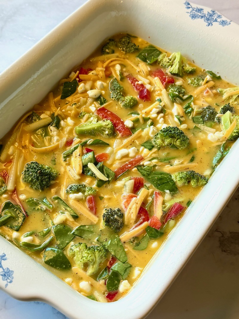 Egg mixture combined with cottage cheese, veggies, seasonings, hash browns and cheese in a casserole dish.