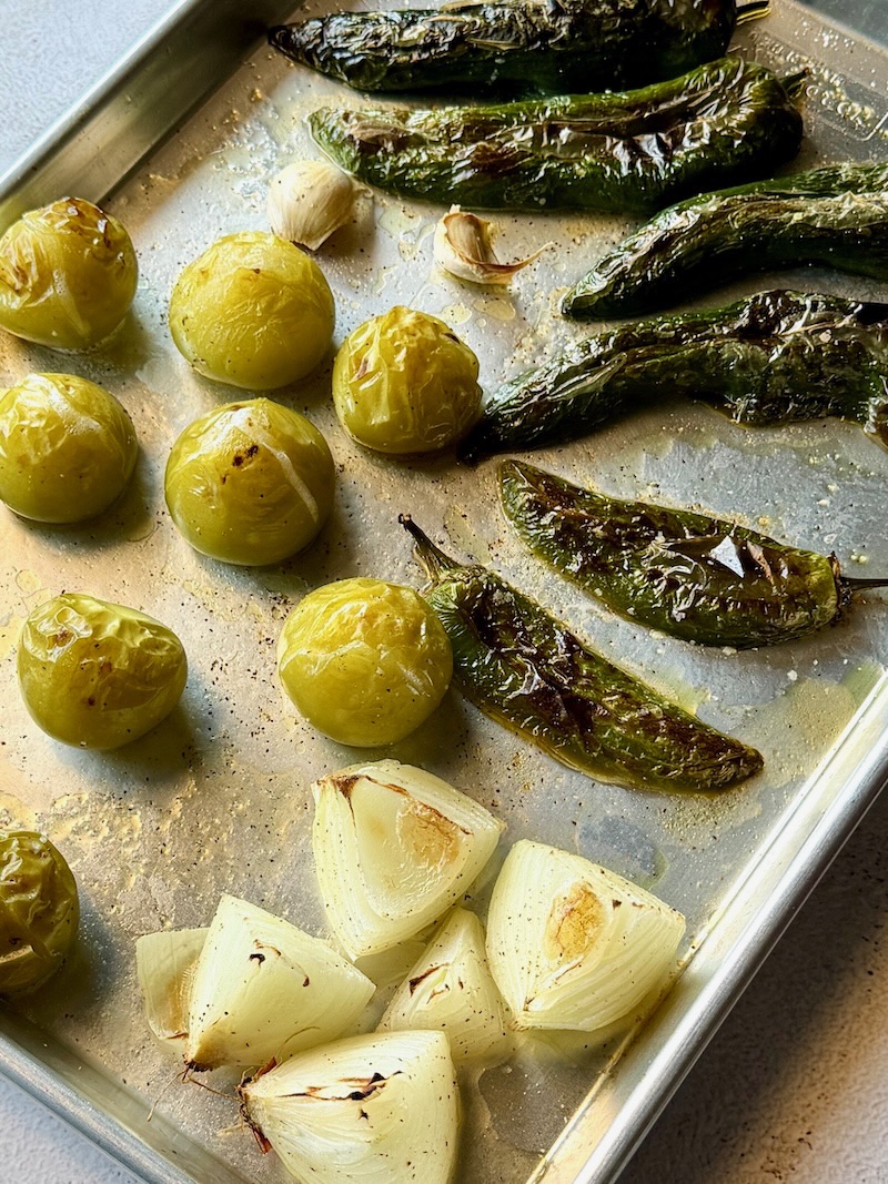 Peppers, onions, garlic, and tomatillos roasted on a sheet pan with olive oil.