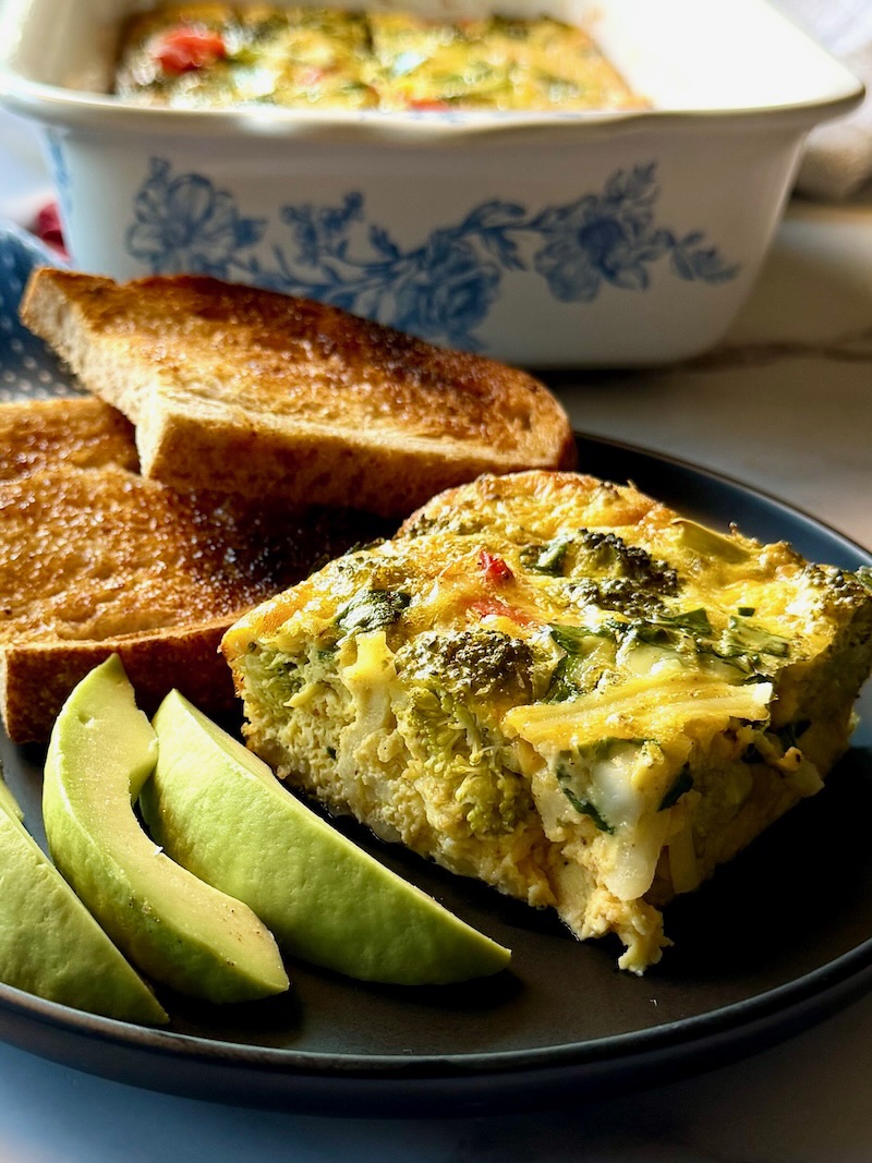 A plate with a serving of breakfast casserole, fresh avocado slices, and toast. 