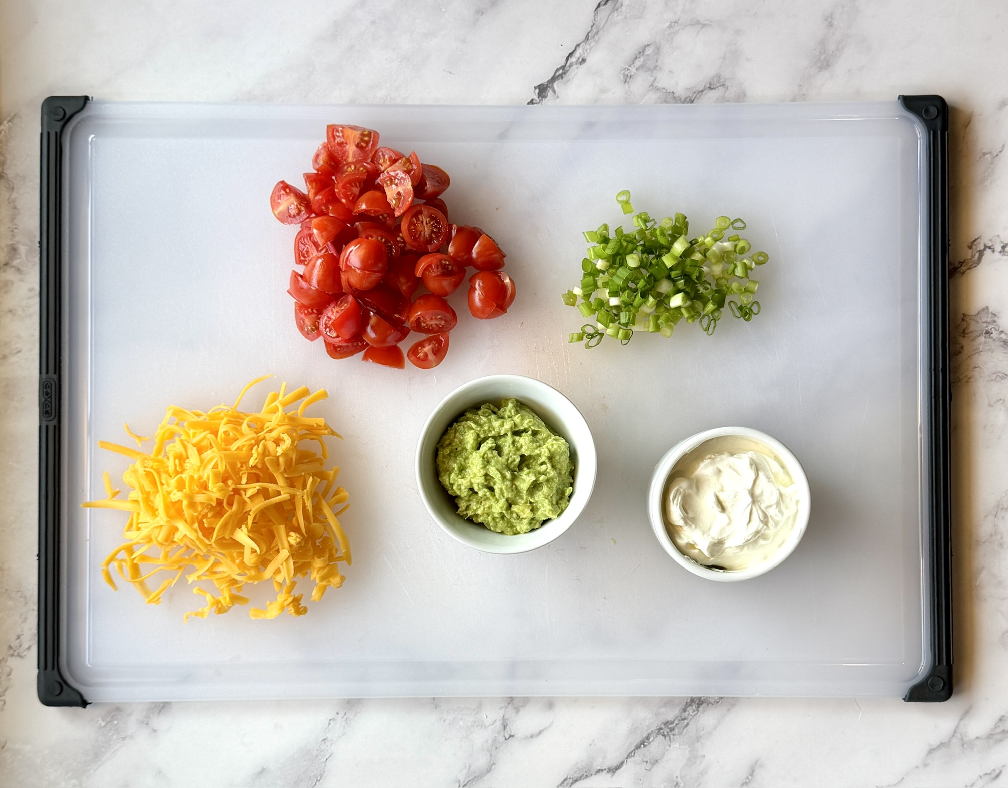 Toppings for taco sweet potatoes--tomatoes, green onions, sour cream, smashed avocado, and cheese. 