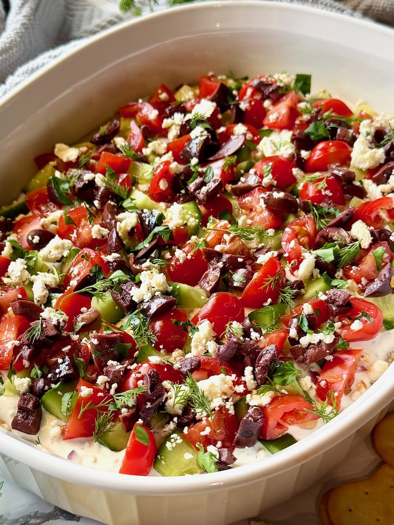 Hummus and tzatziki topped with tomatoes, cucumbers, olives, feta cheese, and herbs.