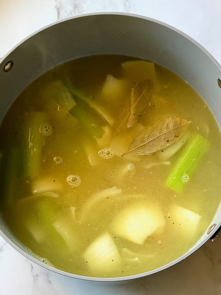 Vegetables, chicken broth, bay leaves, and parmesan cheese rind in a large soup pot.