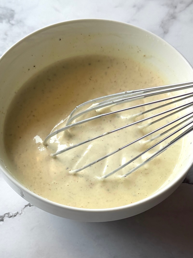 Dressing ingredients combined in a bowl with a whisk.