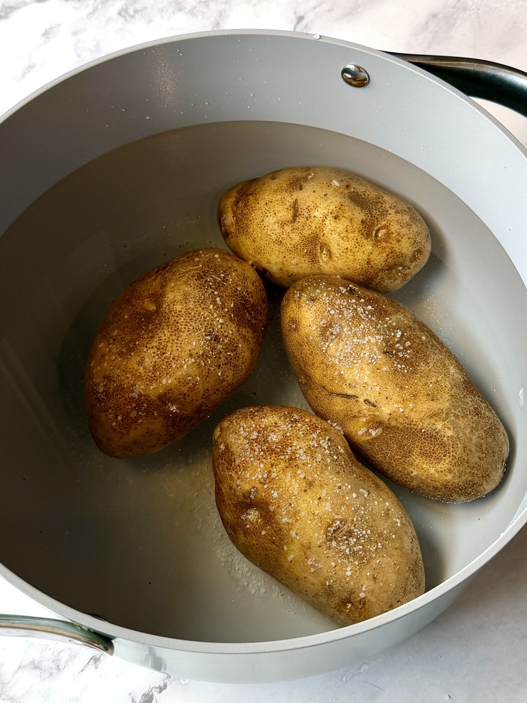 Whole russet potatoes, unpeeled in a pot of water with salt.