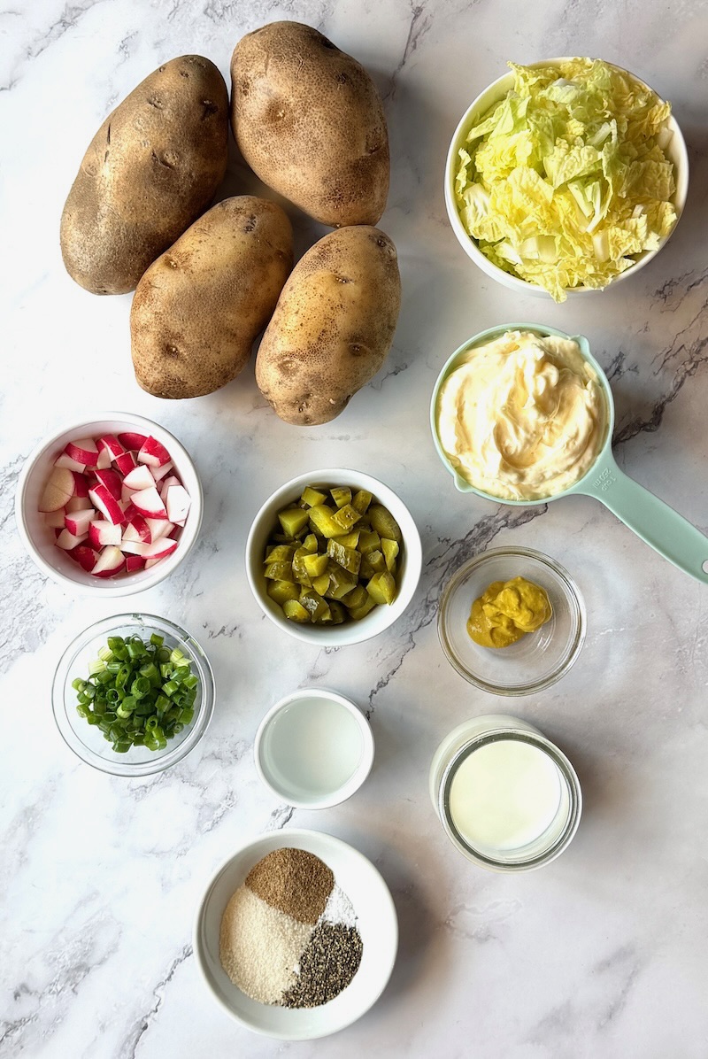 Ingredients displayed for Irish potato salad with cabbage. Russet potatoes, green cabbage, radishes, dill pickles, green onions, mayo, mustard, white vinegar, milk, and pantry seasonings. 