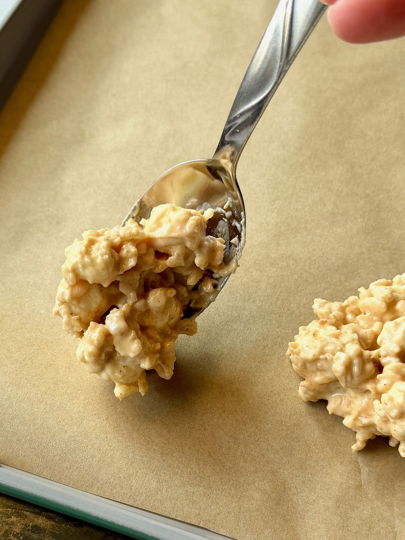 A spoon forming cookies on a sheet pan with parchment paper. 