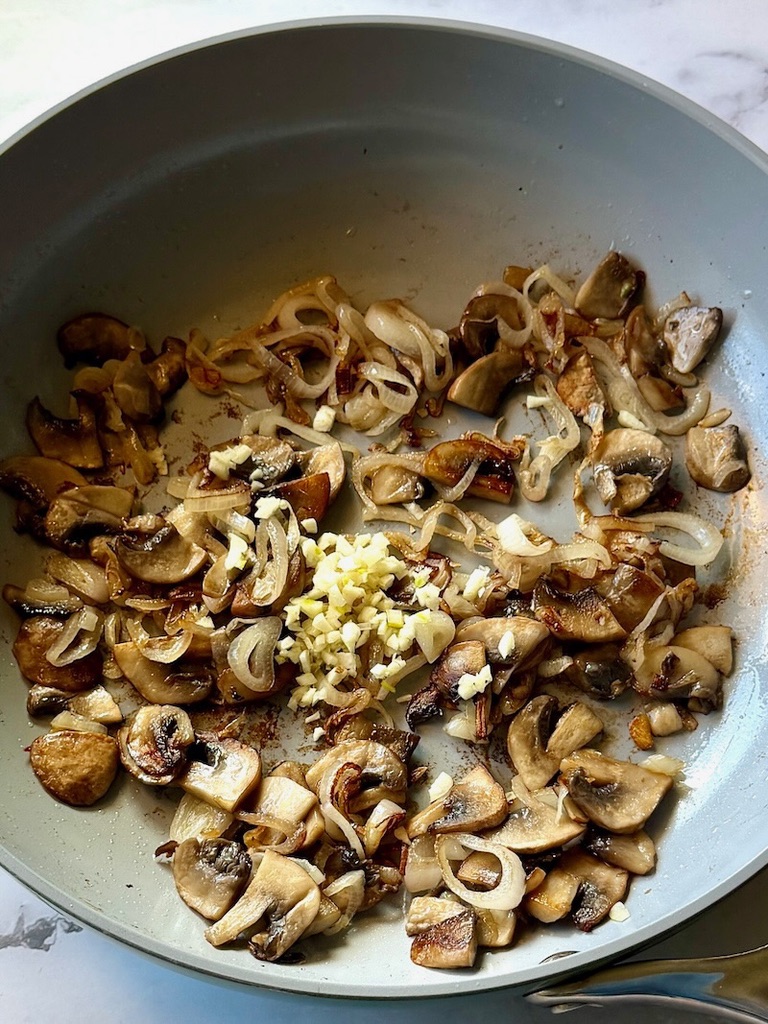 Garlic added to the mushrooms and shallots in a skillet.