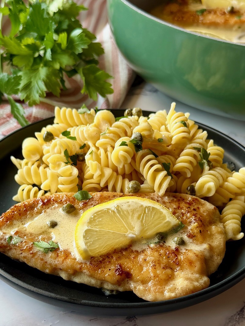 Chicken piccata plated with lemon sauce and pasta. 