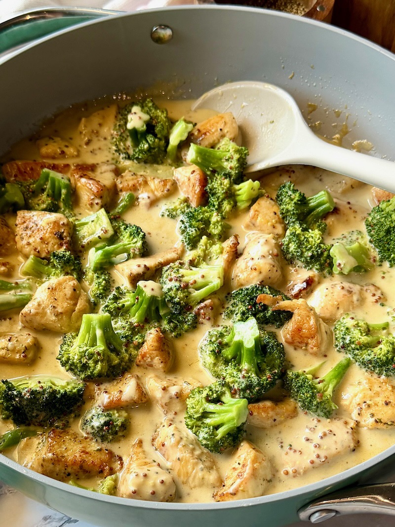 honey mustard chicken and broccoli in a skillet with a serving spoon. 
