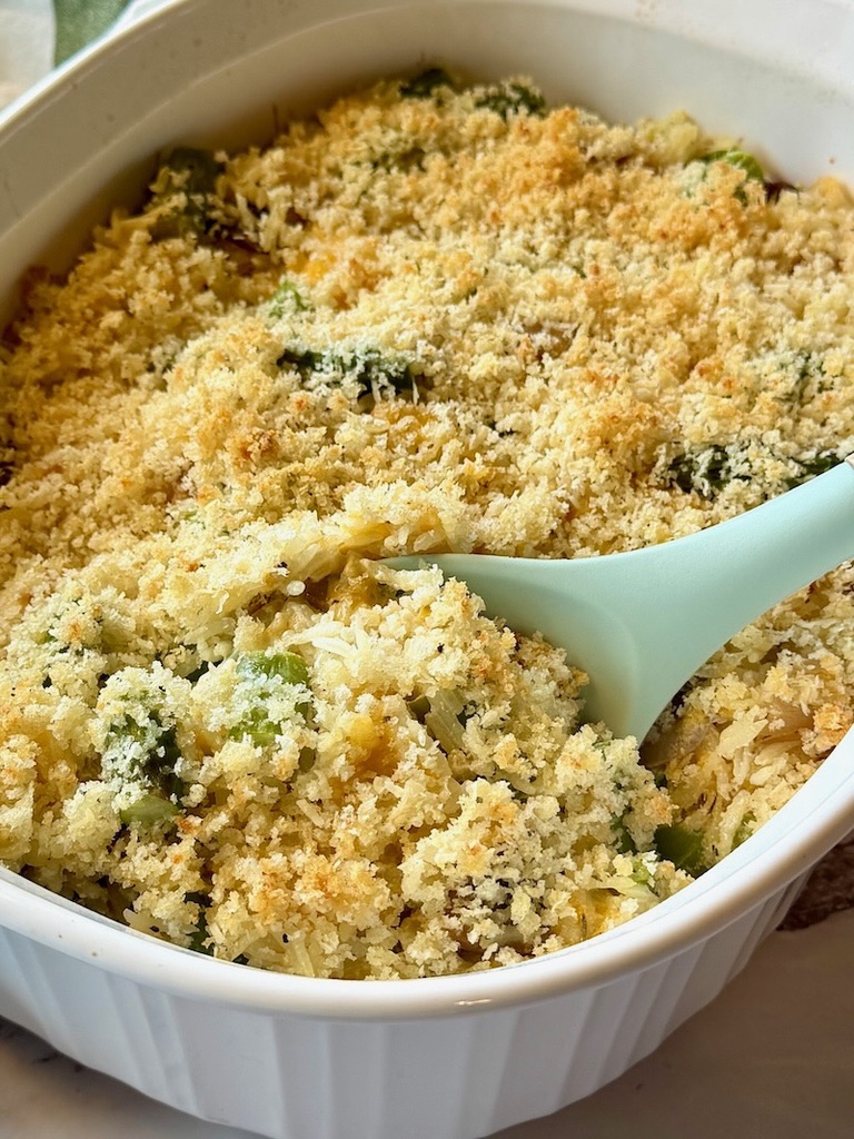 Cheesy asparagus rice casserole baked with a serving spoon. 
