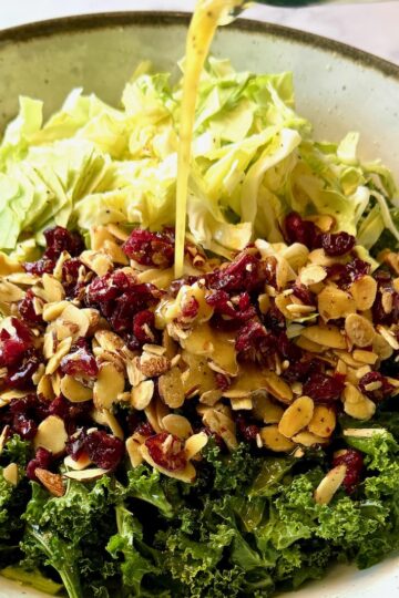 Kale, cabbage, almonds, cranberries, and dressing in a bowl.