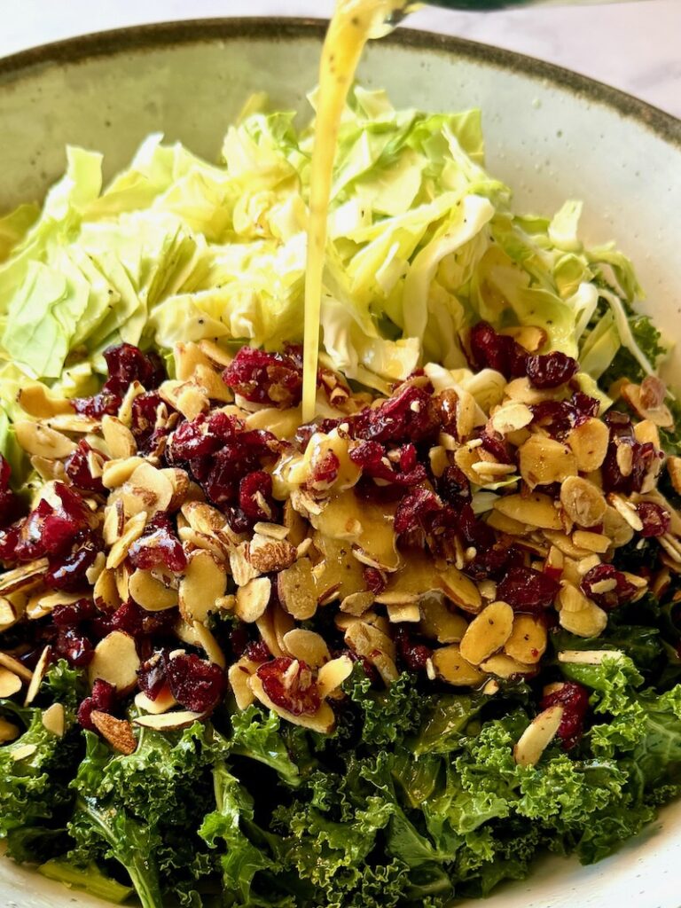 Kale, cabbage, almonds, cranberries, and dressing in a bowl.
