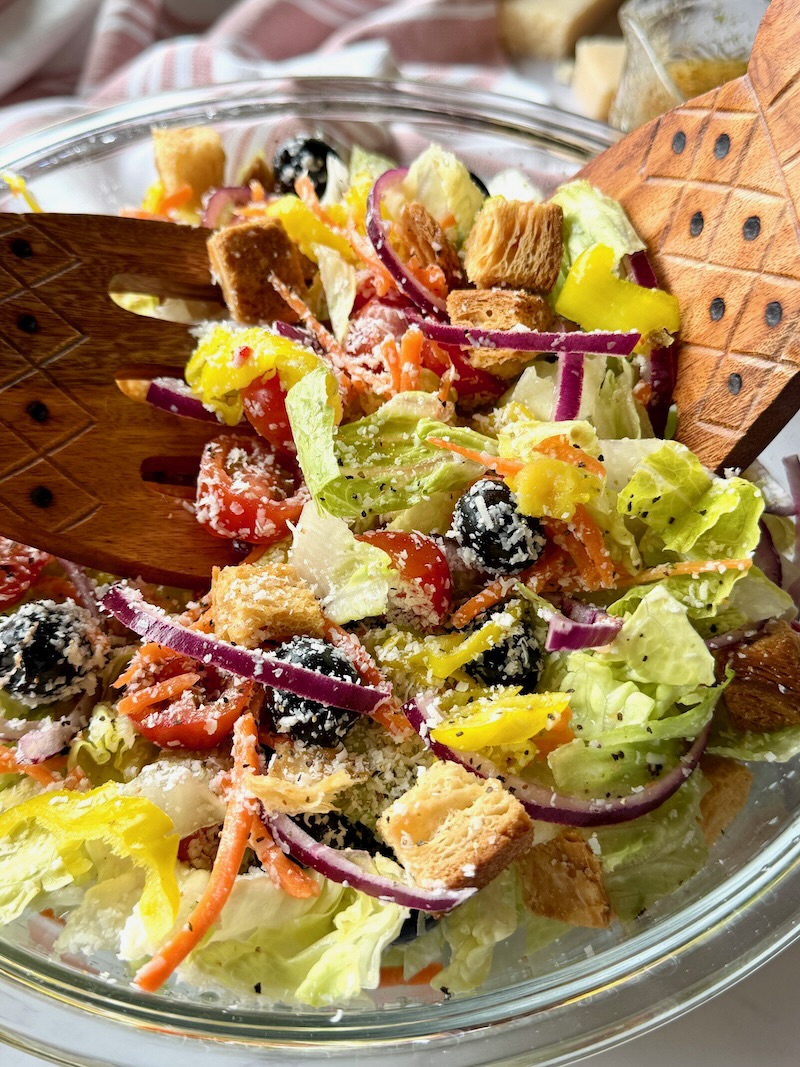 Olive garden salad in a serving bowl with tongs.
