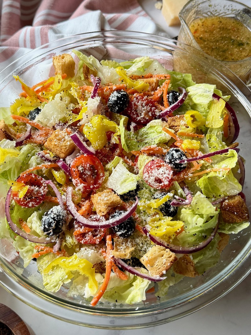 Olive garden salad mixed together with dressing in a serving bowl