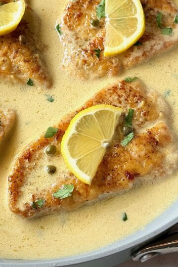 Chicken piccata with lemon butter sauce with fresh lemons on top in a skillet