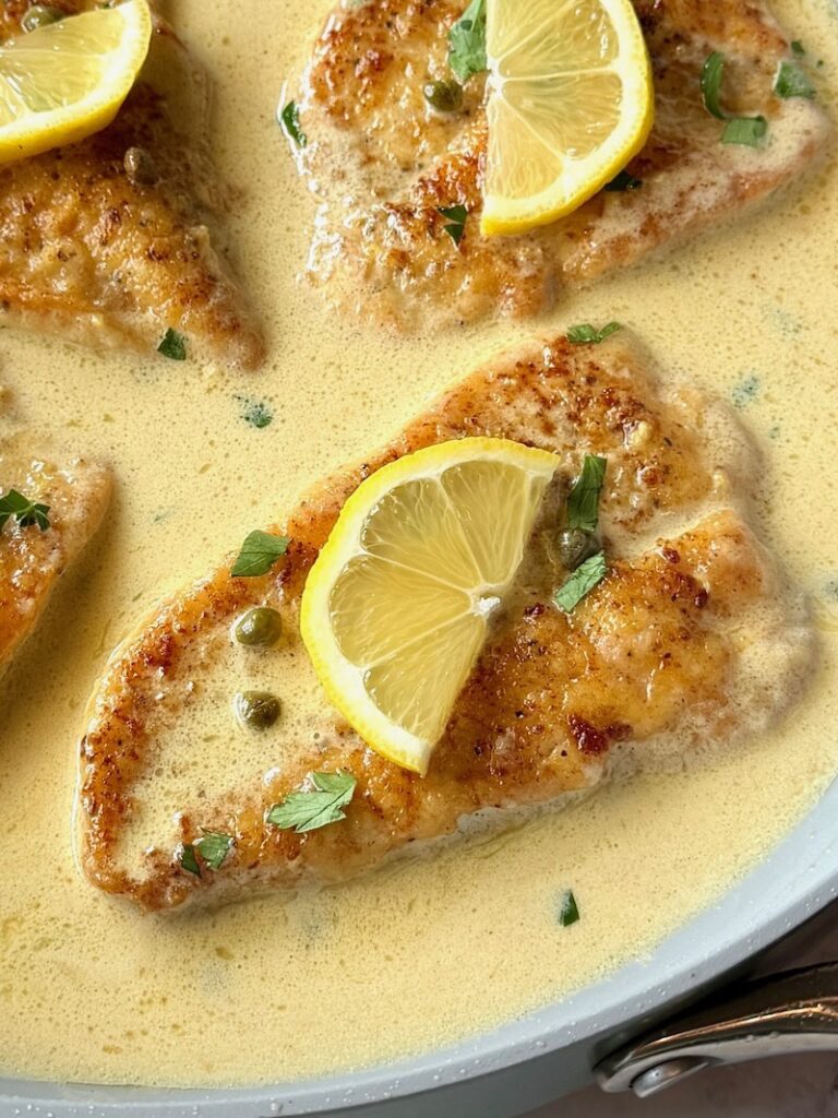 Chicken piccata with lemon butter sauce with fresh lemons on top in a skillet
