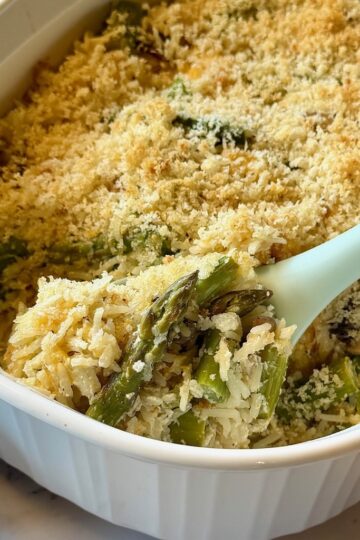 Cheesy Asparagus and rice casserole with a serving spoon.