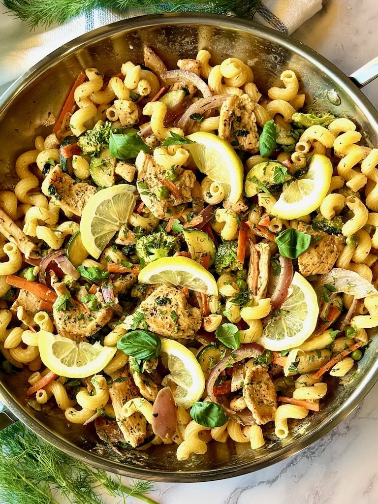 Chicken primavera cooked in a skillet with fresh lemon wedges on top.