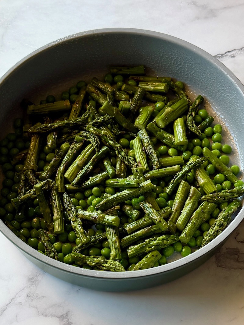 Roasted asparagus cut and put in a round baking pan with thawed green peas.
