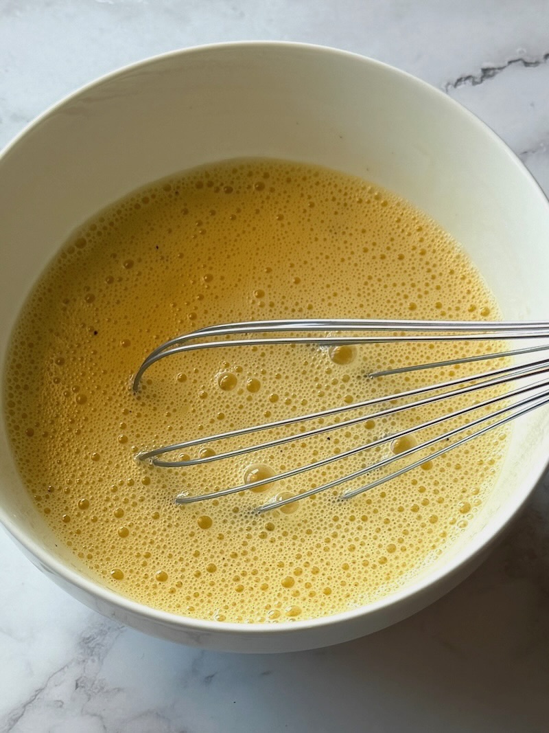 Eggs, milk, salt and pepper combined in a mixing bowl.