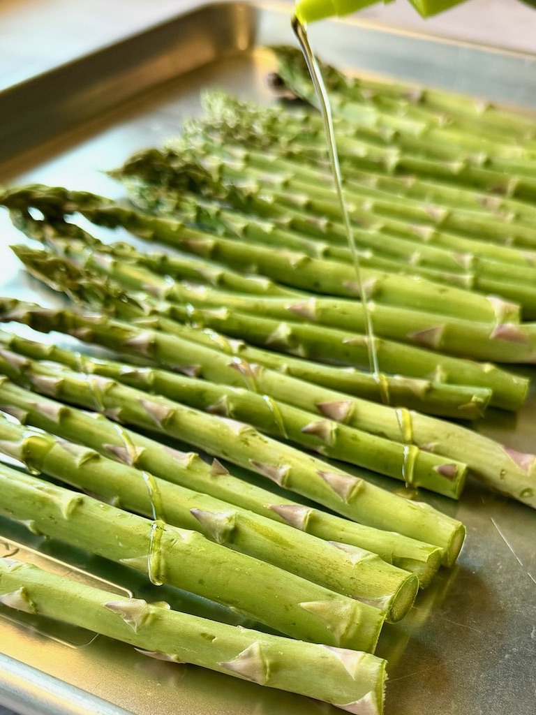 Asparagus on a sheet pan drizzled with olive oil. 