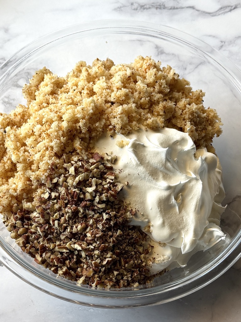 Whipped cream, crushed macaroons, and pecans in a bowl.