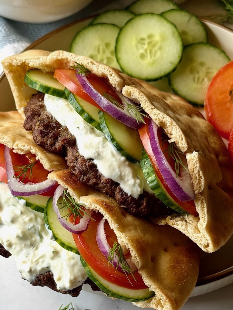 Greek pita burger on a plate with cucumbers and tomatoes