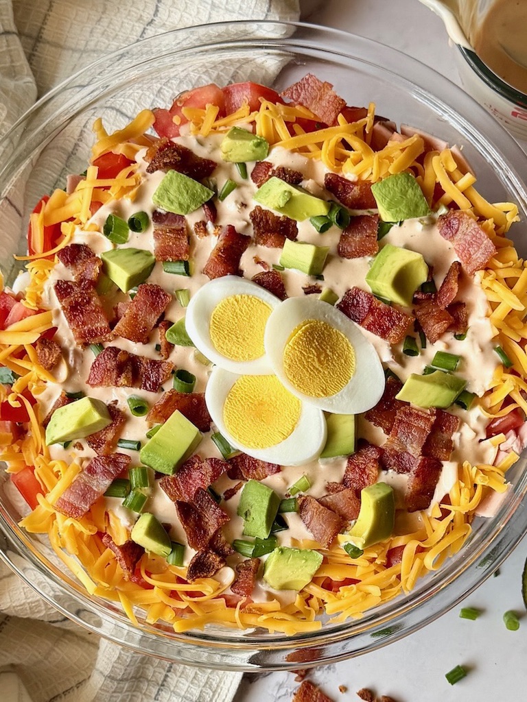 Top view of the layered salad with hard boiled egg, crispy bacon, and avocado.