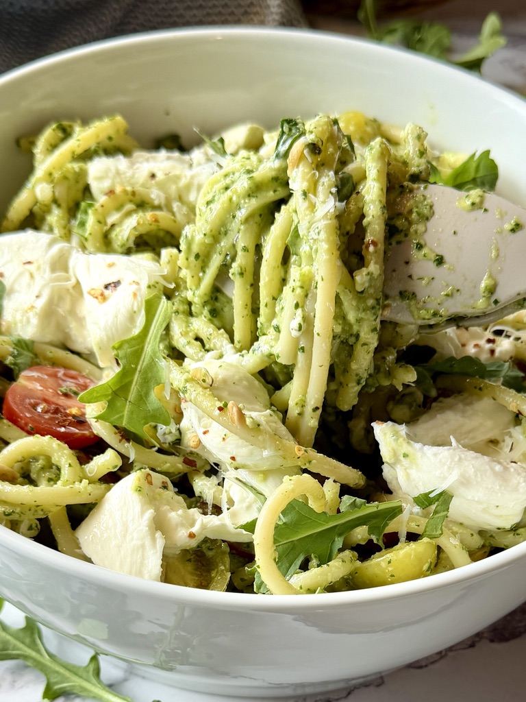 Bucatini arugula pesto in a serving bowl with tongs. 