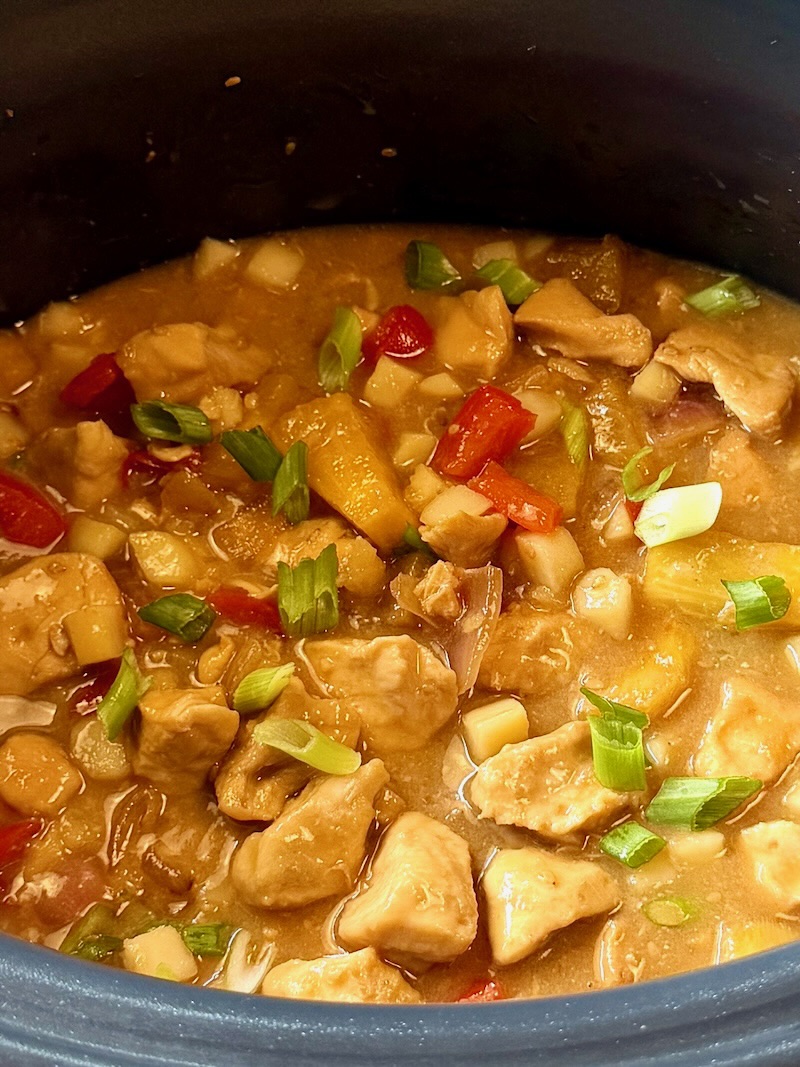 slow cooker pineapple chicken in the crockpot fully cooked and topped with green onions. 