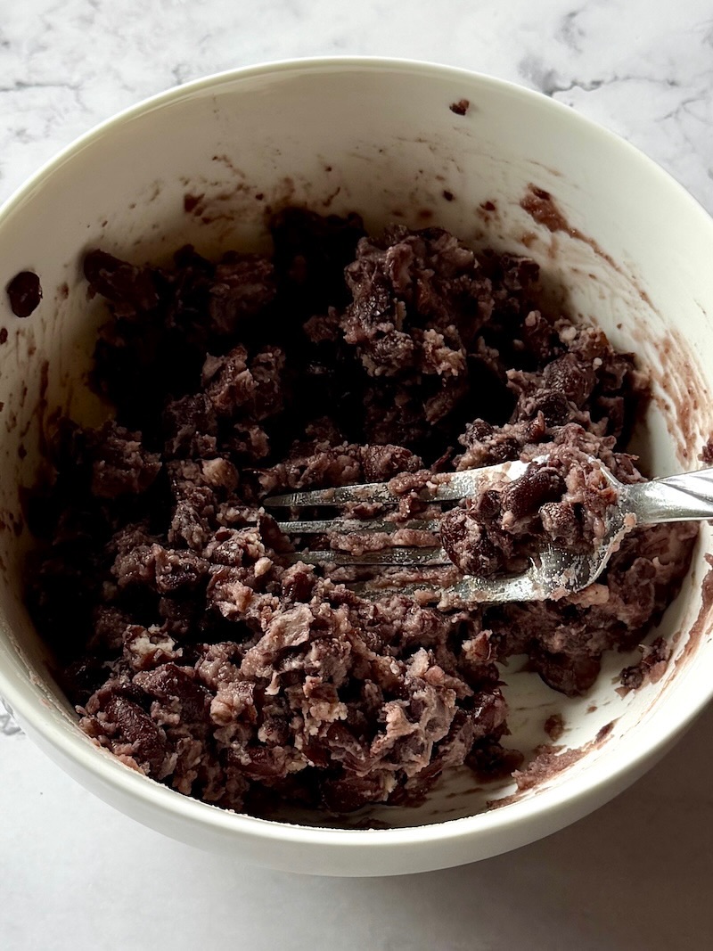 smashed black beans in a bowl with a fork