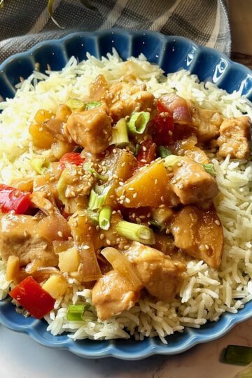 Pineapple chicken over rice and served on a plate.