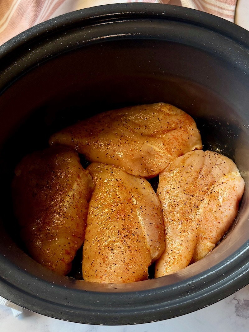 Raw chicken in the slow cooker with olive oil and seasonings. 